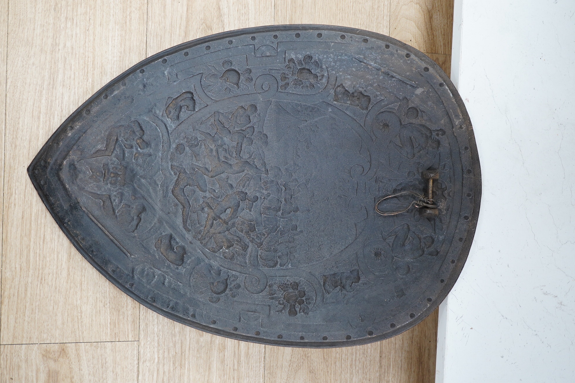 A decorative late 19th century cast iron shield in a romantic style, scene incorporates classical battles surrounded by masks captives, cannon and fruit, 60 x 42.5cm. Condition - good